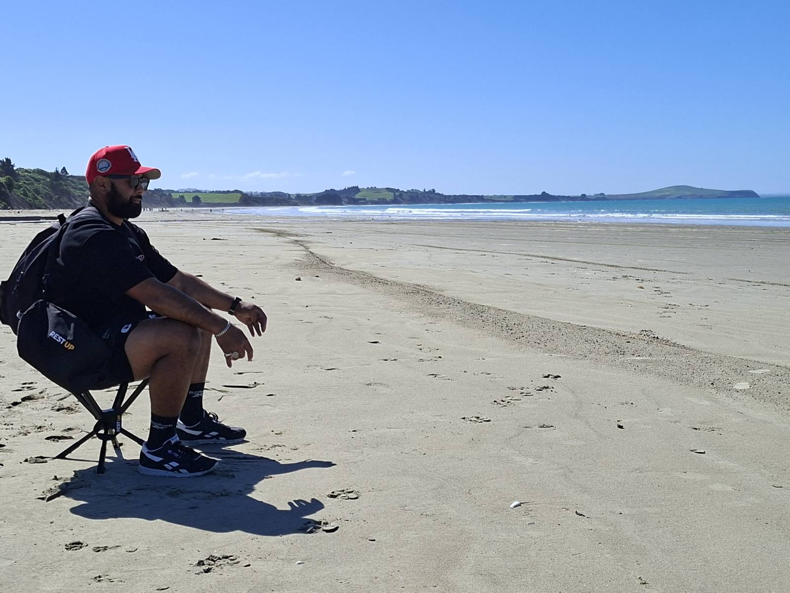 Sitting on the Restup portable seat on a beach, with the carry bag worn as a backpack