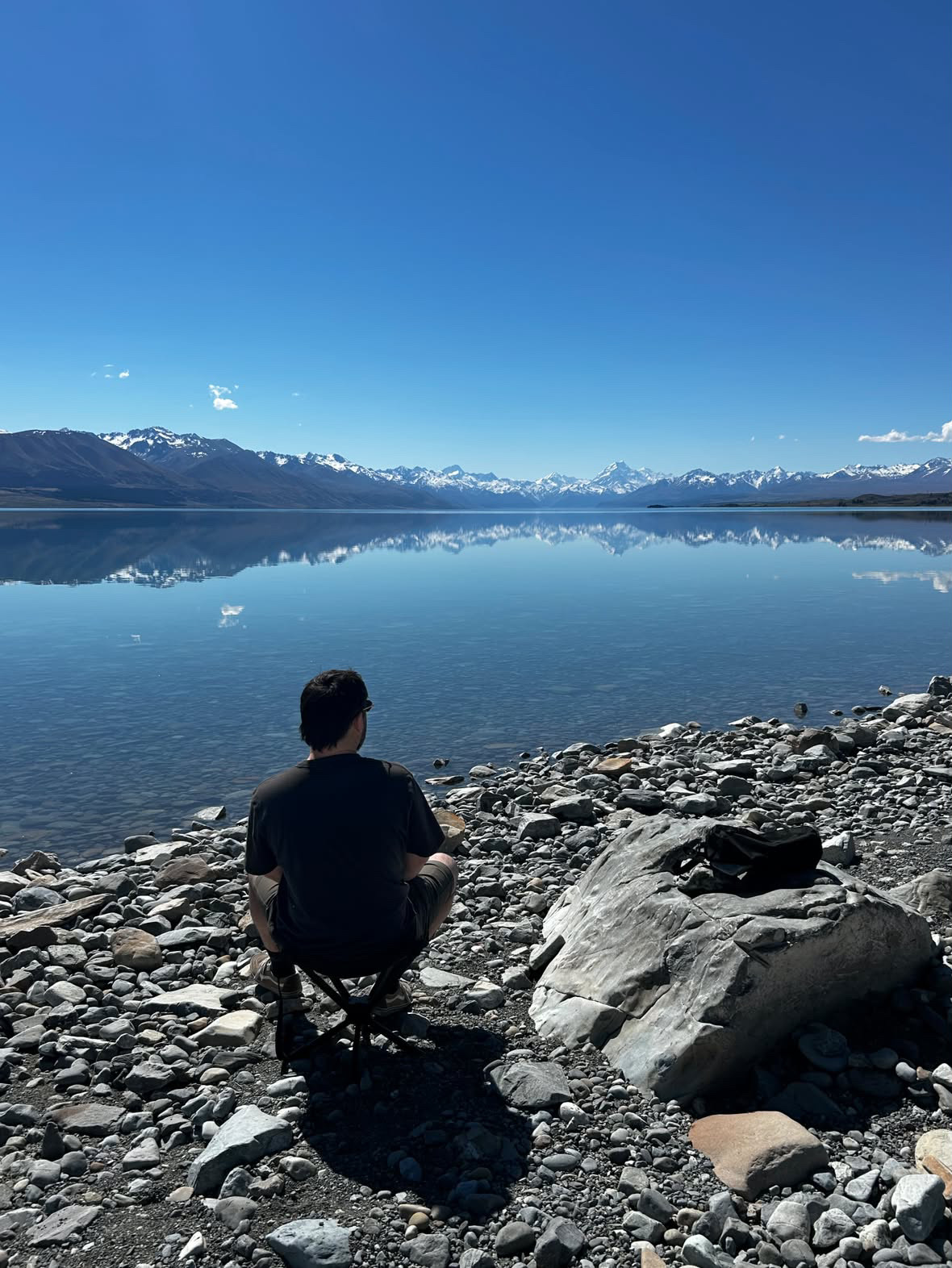 Customer photo: sitting on a Restup seat on the stony shore of an alpine lake with snowy mountains behind